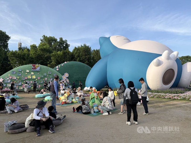 「寶可夢花徑漫遊」活動巨大卡比獸旁邊的草地上擺放許多寶可夢懶人沙發，許多大小朋友愜意地躺臥在沙發上，和卡比獸一起享受春日陽光。中央社記者廖文綺上海攝　115年5月8日