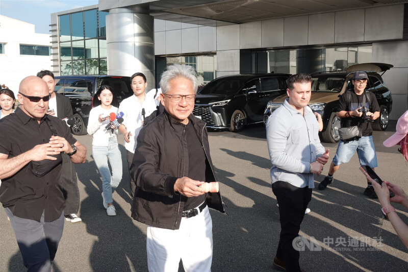輝達執行長黃仁勳(中)23日下午搭乘私人專機抵台,步出松山機場商務中心時,分發養樂多給現場守候的媒體與粉絲。中央社記者吳書緯攝 115年5月23日