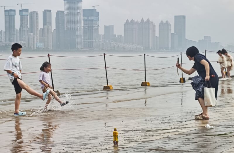 中國武漢市一處親水平台23日因長江水位上漲而遭淹沒，有孩童與家長在該處踩水。（中新社）