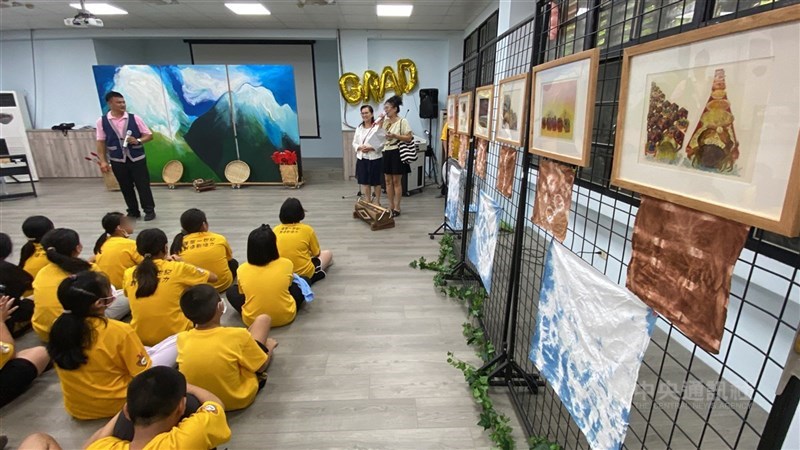 宜蘭縣南澳鄉婦女會理事長王麗萍(立者右2)規劃畫展「來自沖繩石垣島的傳說」,29日在蘇澳蓬萊國小揭幕,校長彭佳志(立者左)與學童出席。 中央社記者黃旭昇攝 115年5月30日