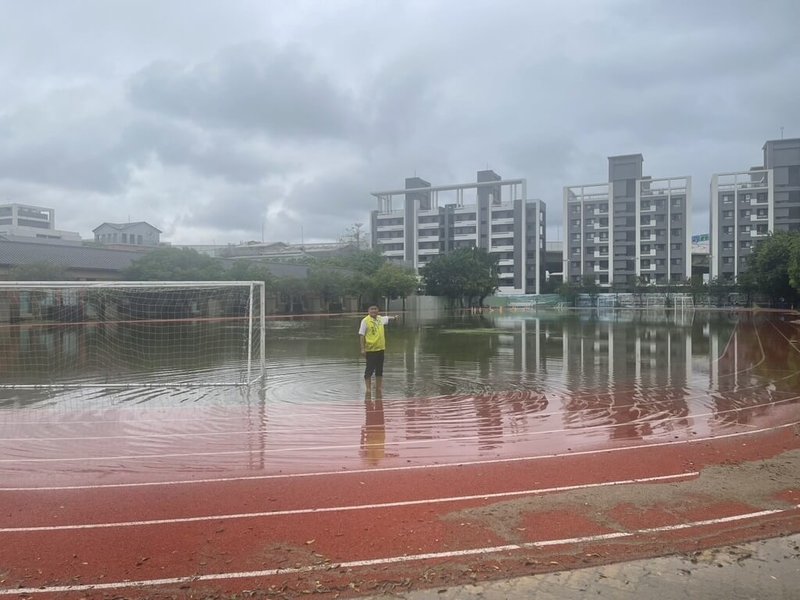 台中清水國小操場積水嚴重，水面可清楚看見一旁建築倒影。民進黨籍台中市議員楊典忠（圖）穿著雨鞋走進積水，指積水不退顯示排水系統明顯出問題。（楊典忠提供）中央社記者趙麗妍傳真　115年6月10日