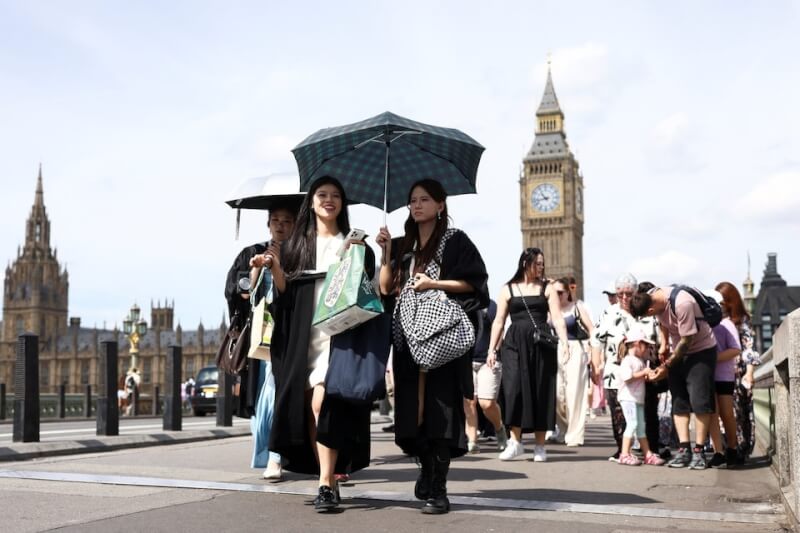 英國倫敦民眾21日撐著陽傘走過西敏橋。(路透社)