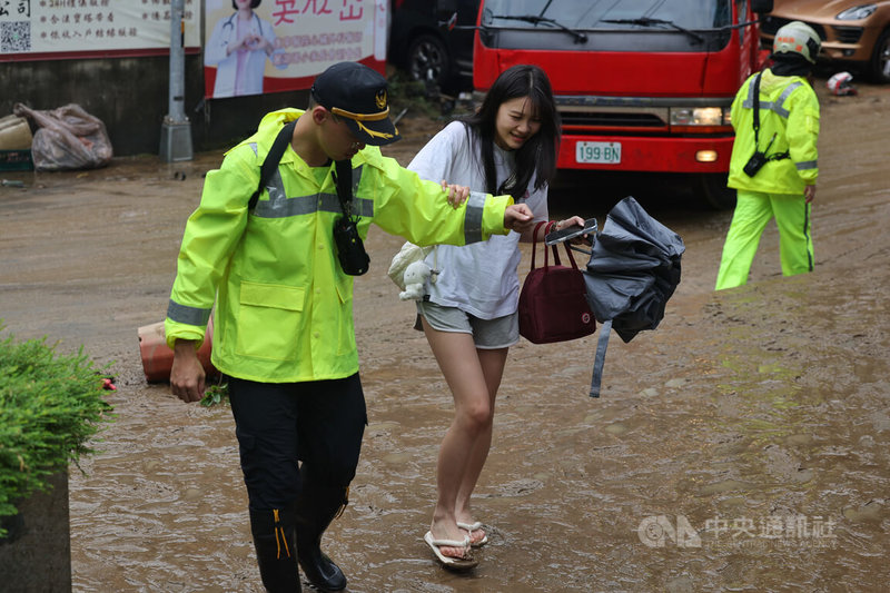 受颱風米克拉影響，台北市25日上午降下大雨，雨勢集中在中山、內湖、松山、信義及南港區，圖為內湖地區積水退去後，消防人員攙扶行走在泥濘道路上的民眾。中央社記者王飛華攝　115年6月25日