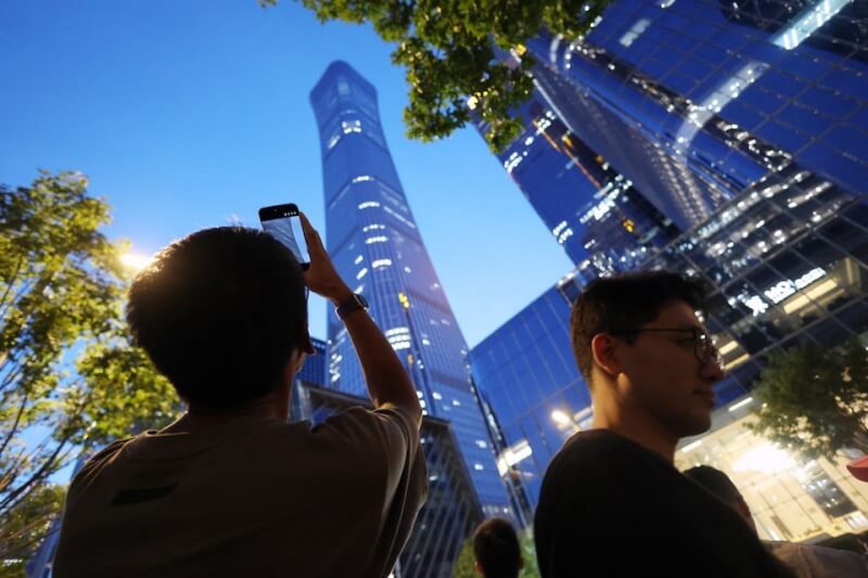 圖為26日一名男子拿手機拍「中國尊」大樓。（路透社）