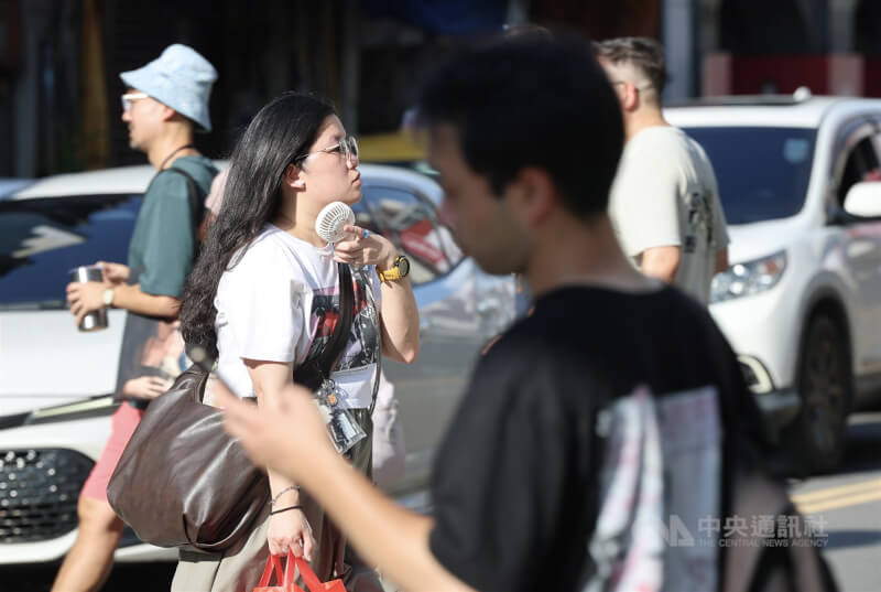 台北市大同區街頭民眾隨身攜帶微型風扇消暑。（中央社檔案照片）