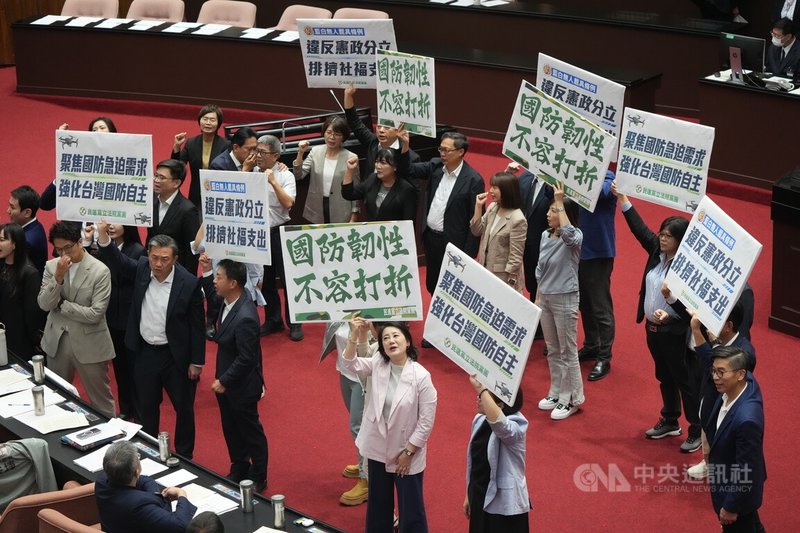 立法院3日上午召開院會，在處理報告事項時，朝野黨團無異議，將國民黨團所提「國防自主無人載具科技發展及採購條例草案」、民眾黨團所提「強化國防自主暨無人機產業發展條例草案」，交付立法院經濟、外交及國防、財政3委員會審查。圖為民進黨立委在議場中舉牌喊口號表達立場。中央社記者徐肇昌攝　115年7月3日