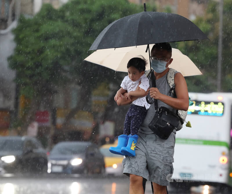 台北市信義區民眾抱著小孩撐傘遮擋雨勢走過馬路。（中央社檔案照片）
