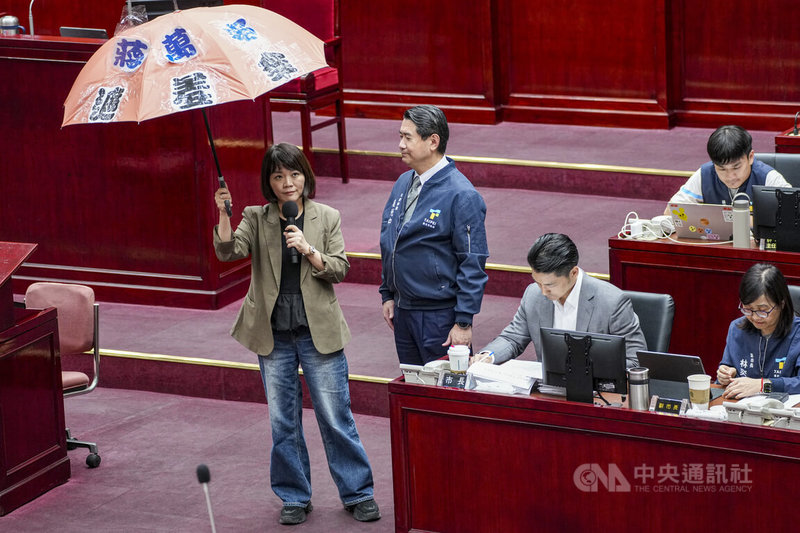 民進黨台北市議員簡舒培(左)16日質詢時拿出「遮羞傘」,質疑市府人行道遮陽設施設置費用大幅增加,卻未提出合理說明,並批評市府將議員索取資料視為政治攻擊,藉此閃躲監督。中央社記者鄭清元攝 115年7月16日