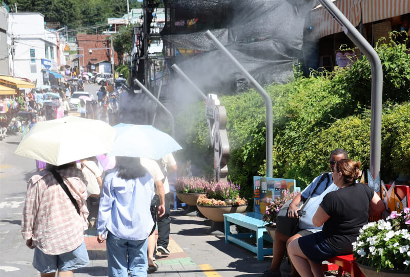 韓國內政部4日表示，今夏全國已有16人因高溫死亡。圖為南韓釜山街頭灑水降溫，民眾撐傘避暑。（韓聯社）