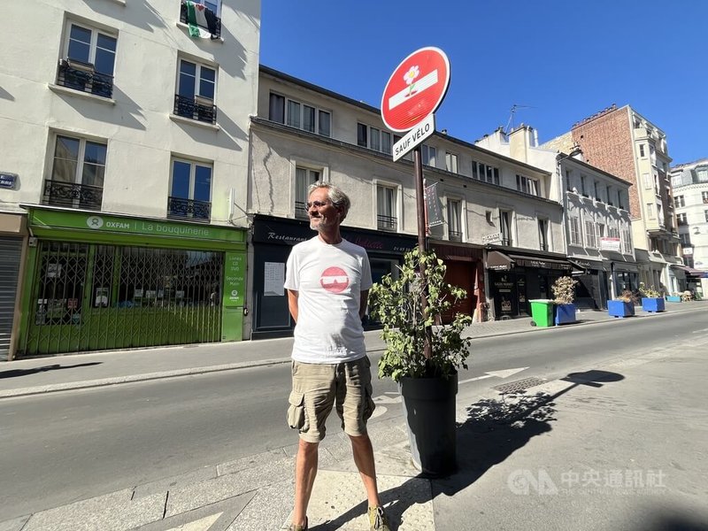 法國街頭藝術家亞伯拉罕（Clet Abraham）近日在巴黎街頭與他剛完成的貼紙藝術創作合影。他將粉紅花朵貼紙黏在「禁止通行」路標的白色橫槓上，表達人們需要自由的空間。中央社實習記者洪嘉琪巴黎攝　115年8月15日