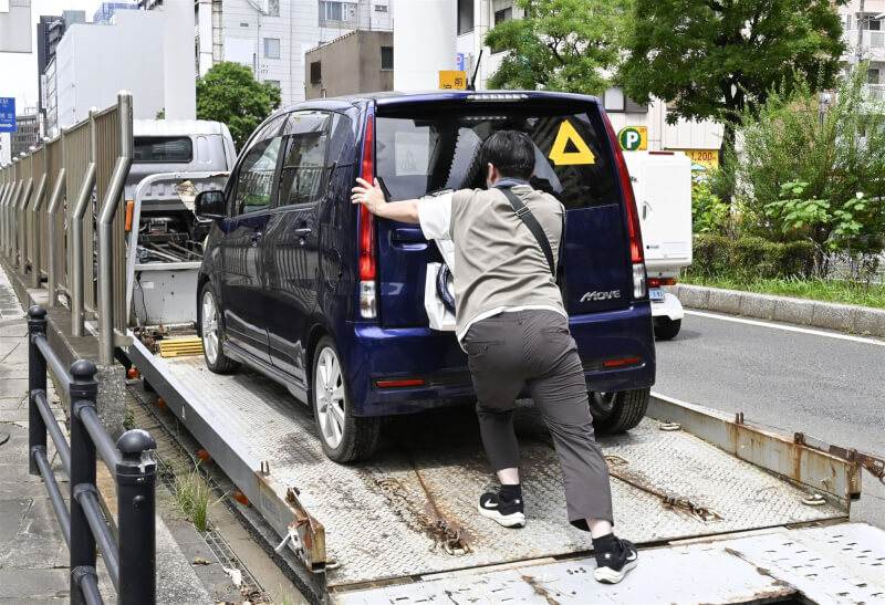 日本千葉縣約2700輛車因豪雨被棄置在路上。一名男子將泡水車裝上汽車運輸車。（共同社）