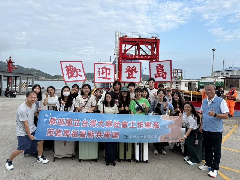 為解決連江縣南竿鄉暑期幼童托育困難狀況，由家長自主發起的共學營今年邁入第2年，在唐氏症基金會媒合下，17名台灣大學社會工作學系學生日前跨海抵達馬祖，支援為期5天的共學營，家長們於南竿福澳港舉牌歡迎。（馬祖青年發展協會提供）中央社記者潘欣彤傳真　115年8月20日