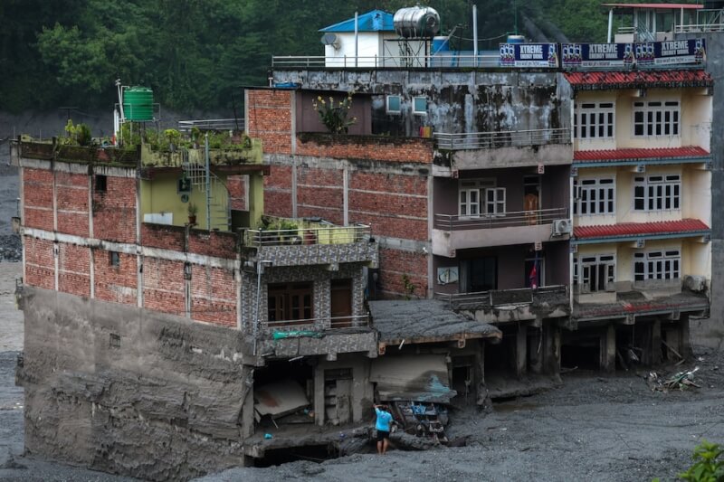 29日尼泊爾努瓦科特地區一名男子站在因洪災毀損的建築物前。（路透社）