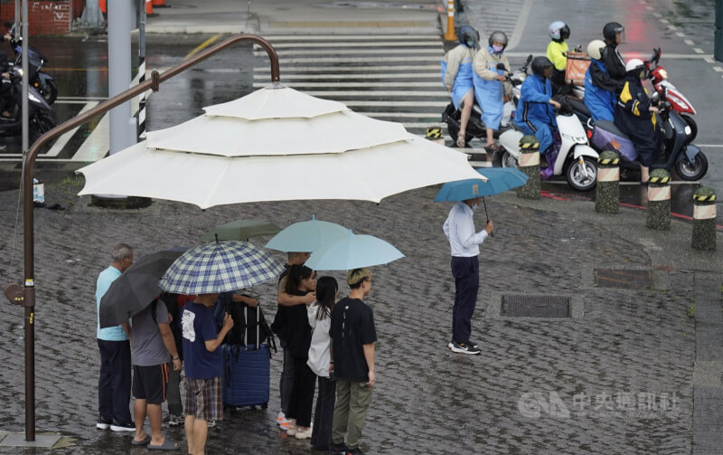 圖為8月31日高雄市前鎮區下起陣雨，行人撐傘、機車騎士穿起雨衣遮擋雨勢。（中央社檔案照片）