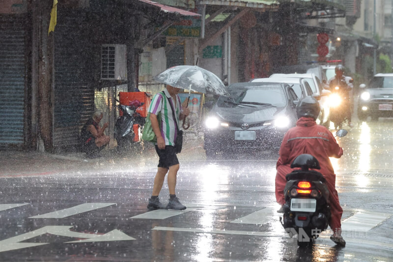 台北市內湖區雨勢滂沱，民眾撐傘通過馬路。（中央社檔案照片）