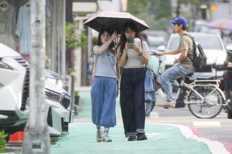 中央氣象署表示，14日起東北季風增強，迎風面的桃園以北、宜蘭與恆春半島要留意局部陣雨。圖為雙北地區午後飄起零星細雨，有民眾一起撐一把傘走在台北街頭。（中央社檔案照片）