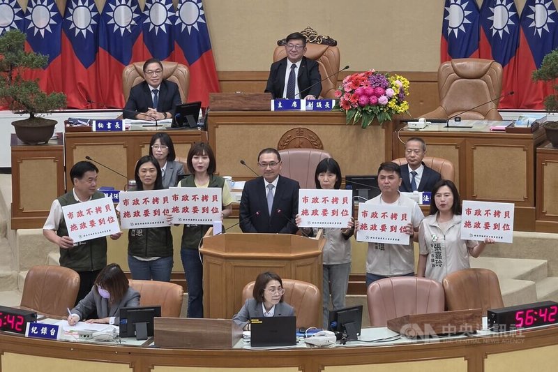 新北市議會16日進行市政總質詢，民進黨議員張嘉玲（2排右起）、廖宜琨、周雅玲等人以「雙北政策比拼」進行聯合質詢，持海報到質詢台向市長侯友宜（2排中）提問，並高喊「市政不拷貝、施政要到位」等口號。中央社記者王鴻國攝　115年9月16日