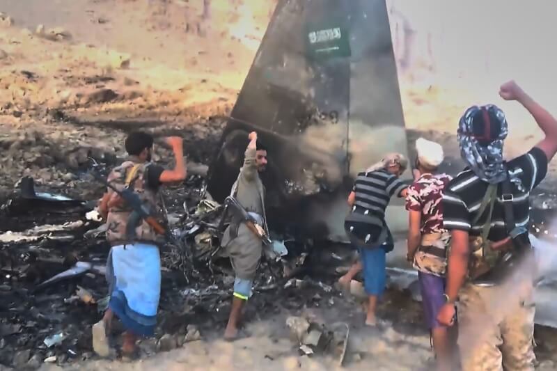 青年運動武裝人員16日在一架被擊落的沙國F-15戰鬥機旁高喊口號、揮舞拳頭。（Ansar Allah Media Office via 美聯社）