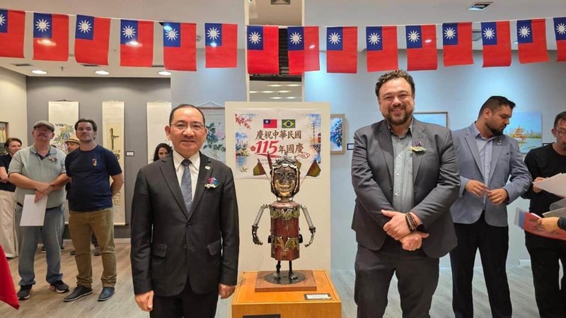 「台巴藝術家聯展」開幕現場，聖保羅華僑文教服務中心主任尤正才（左）與索羅卡巴市文化局長黎貝洛在國慶海報及三太子雕塑前合影，象徵台灣與巴西文化交流的友好合作。（聖保羅華僑文教服務中心提供）中央社記者唐雅陵聖保羅傳真　115年9月20日