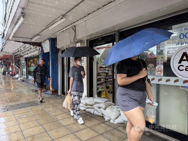 泰國曼谷26日持續降雨，民眾撐傘冒雨外出，超商門口堆放沙包防範淹水。中央社記者李宗憲曼谷攝　115年9月26日