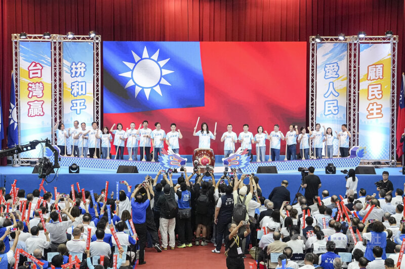 圖為中國國民黨7月25日舉行全國代表大會，黨主席鄭麗文（台上中）與黨籍縣市長參選人在大型國旗圖像前擊鼓高呼，台下與會者揮舞加油棒響應。（中央社檔案照片）