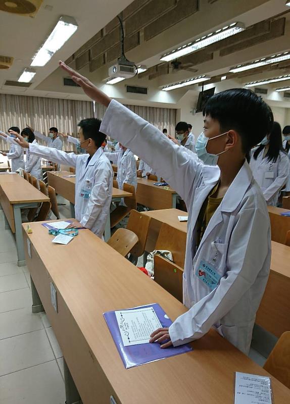 學員身披白袍，高舉右手，宣讀醫學教育誓詞
