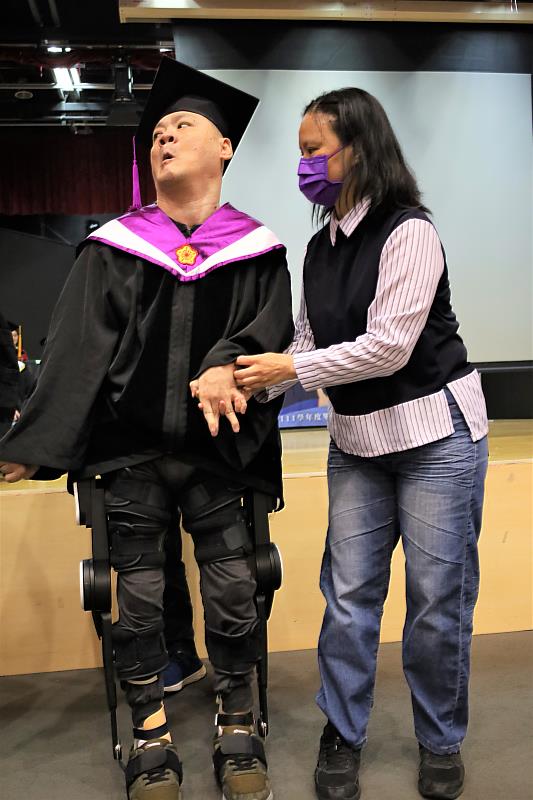 圖為亞大腦麻博士生陳銘哲(左)，穿著「外骨骼機器人」，人生第1次從輪椅站起來，能夠行走，放開大姊陳秀玉手去領獎。