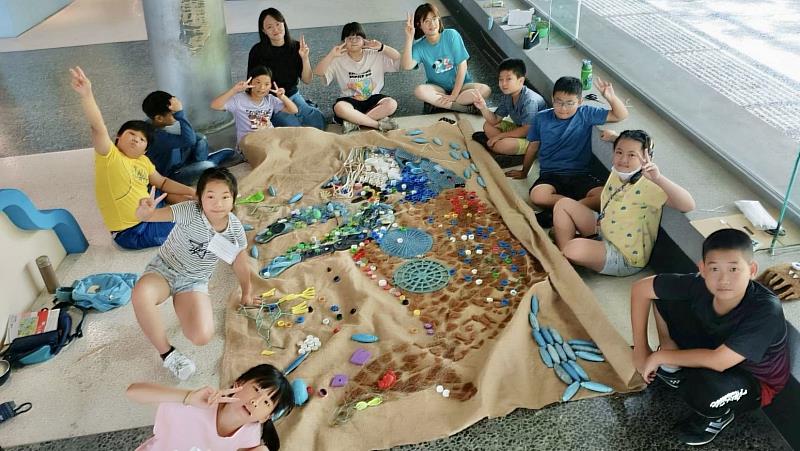 梗枋國小學童及藝術家坐在地上與海廢鯨魚藝術品合照