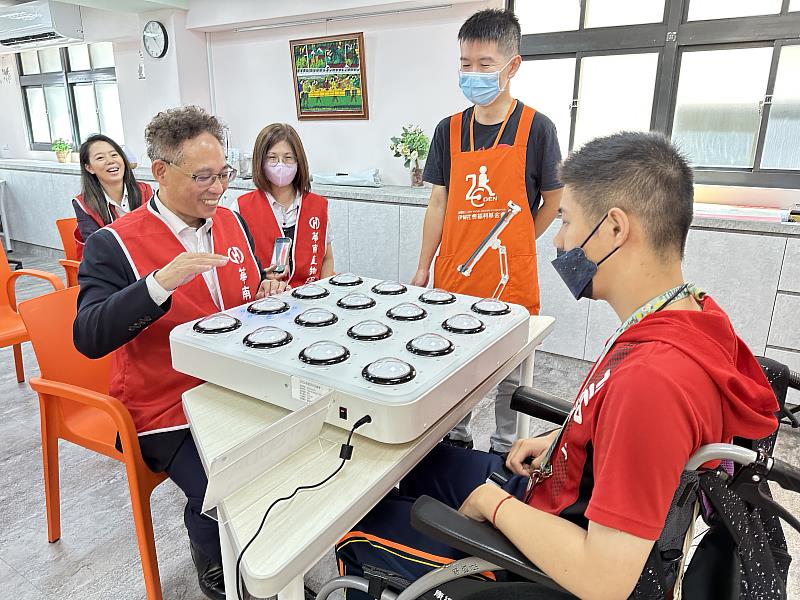 伊甸日照中心的服務對象小毅，帶領華南產險經理張文志體驗「手拍認知訓練機」的樂趣。