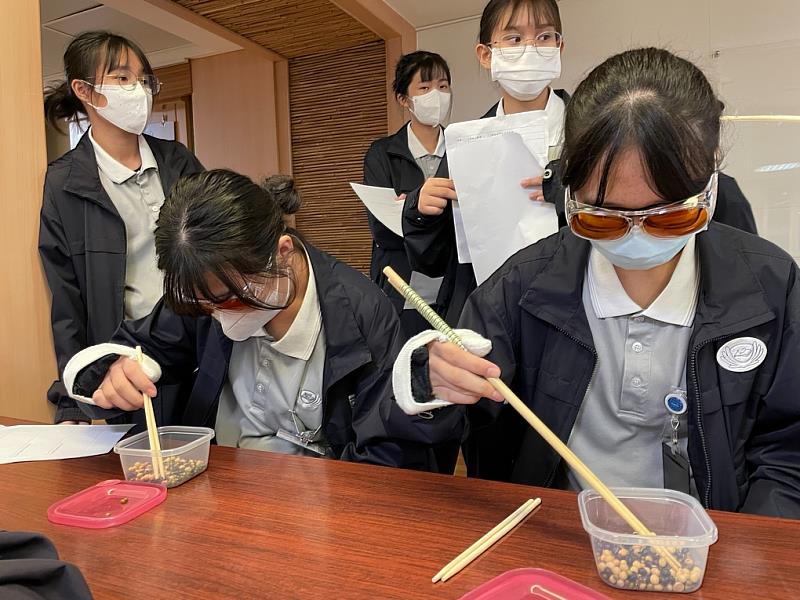 手背綁著沙袋，護理科系學生從夾豆子中，了解病人的手部控制力下降時影響到生活能力。