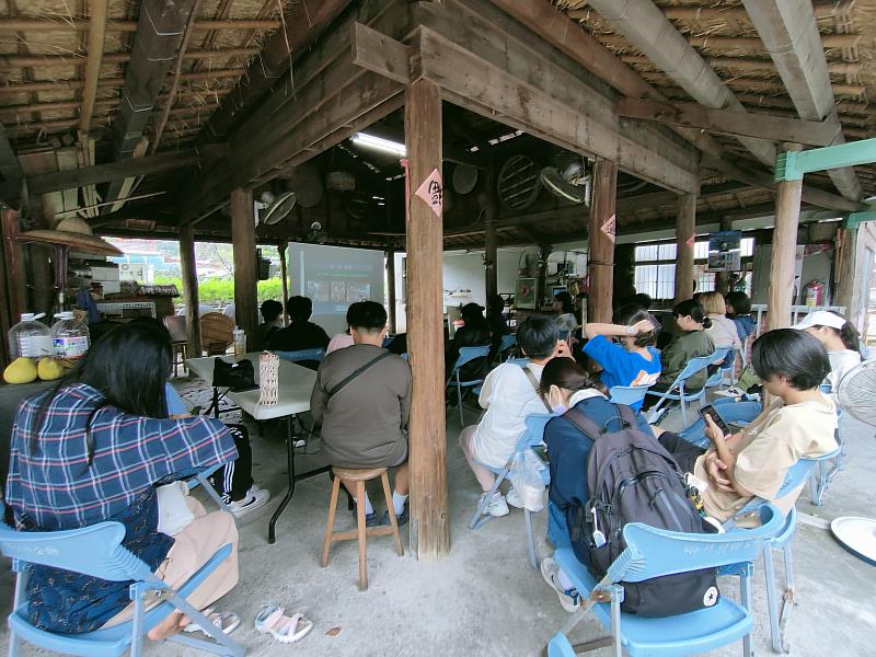 師生在傳統茅草屋下聽取簡報。