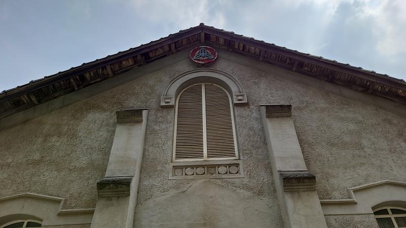 正立面上方有拱形百頁推窗，中間上方有紅色圓盤綠色三竹葉的木製校徽。