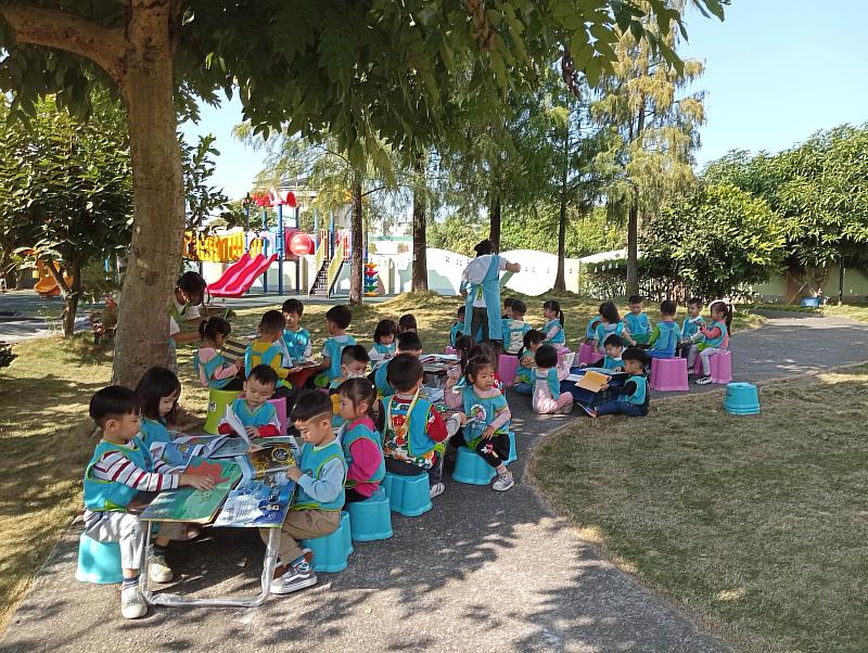 南華大學雲水書車至幼兒園推廣閱讀,孩童聽完故事在大樹下閱讀,分享故事內容。
