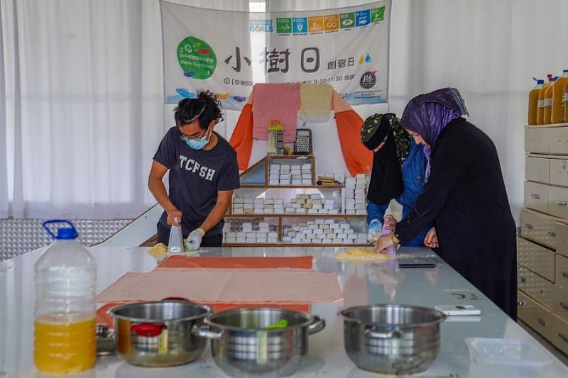 實習生王承恩與製作環保肥皂的婦女一同刨皂絲，為皂乳製作進行準備。