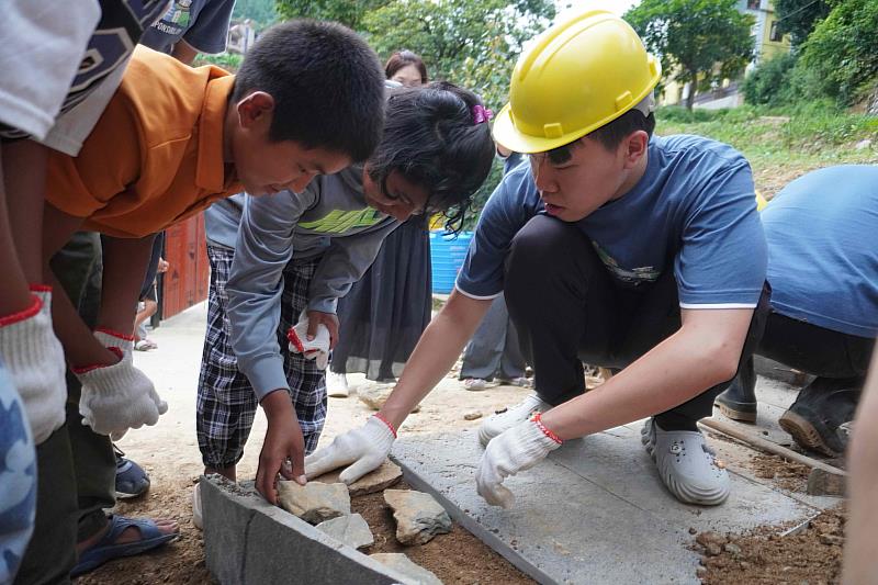 臺科大學生在鋪設手作步道時，與育幼院孩童分享施作的步驟。