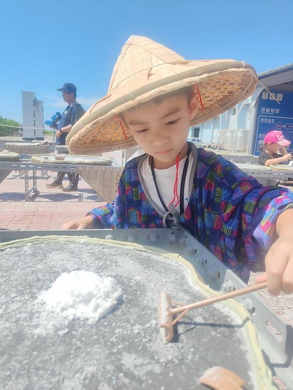 小朋友參加七股鹽山的石板天日曬鹽DIY活動，穿戴斗笠和花袖套，在陽光下耙鹽，了解鹽的製作過程。