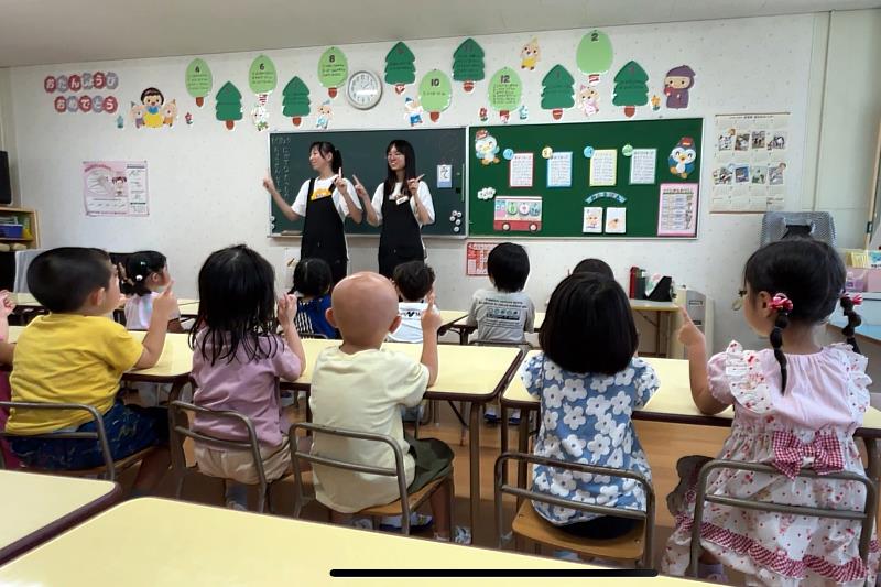 亞大幼教系錢妤蓁（站立者右）、郭曉蓉（站立者左）同學，在日本實習時，以自編手指舞單元教導幼兒律動。