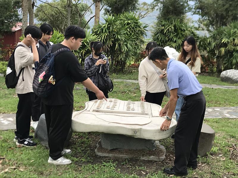 曾富良科長（右側著淺藍色上衣者）跟學生介紹這個由一整塊石材雕成的茶盤及象棋，鼓勵學生玩玩看。