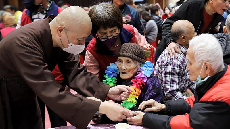 懇慧法師（左）為高齡104歲的人瑞吳綢老菩薩（戴花圈者）繫上象徵隨身平安的五佛珠。（靈鷲山佛教教團提供）