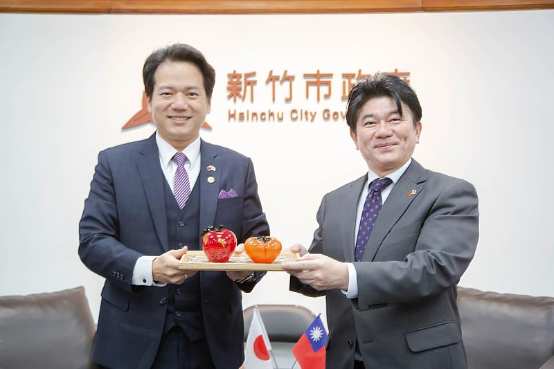 圖2:邱代理市長贈送竹市特色玻璃藝品「一柿蘋安」及米粉禮盒,安部徹也町長也回贈日出町當地名產城下鰈魚的陶器、日本第知名酒廠二階堂所釀燒酒及招福熊手禮品表達感謝之意。