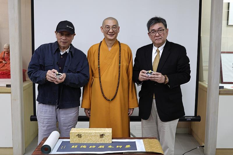 華梵大學校長李天任(右)、泰陽通運公司董事長郭明曉(左)為大慧法師作品「佛手蓋碗」貼上金箔。