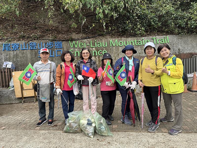 義工夥伴手持國旗與救國團團旗，於高樹鄉尾寮山登山口前合影留念