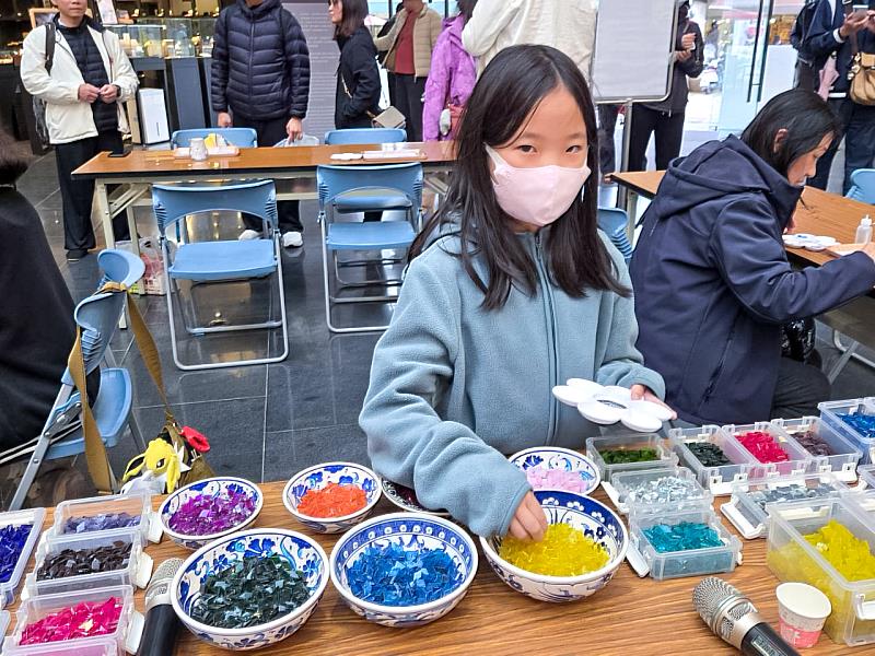 孩子們興奮地在滿桌繽紛的馬賽克玻璃片中挑選喜愛的顏色，為即將誕生的燭台作品增添獨特色彩。