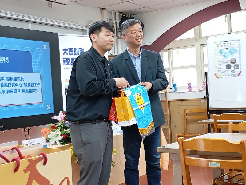 文化大學永續發展暨校務研究中心主任張鈞智與大理高中楊廣銓校長交換錦旗，象徵合作邁向新里程碑。