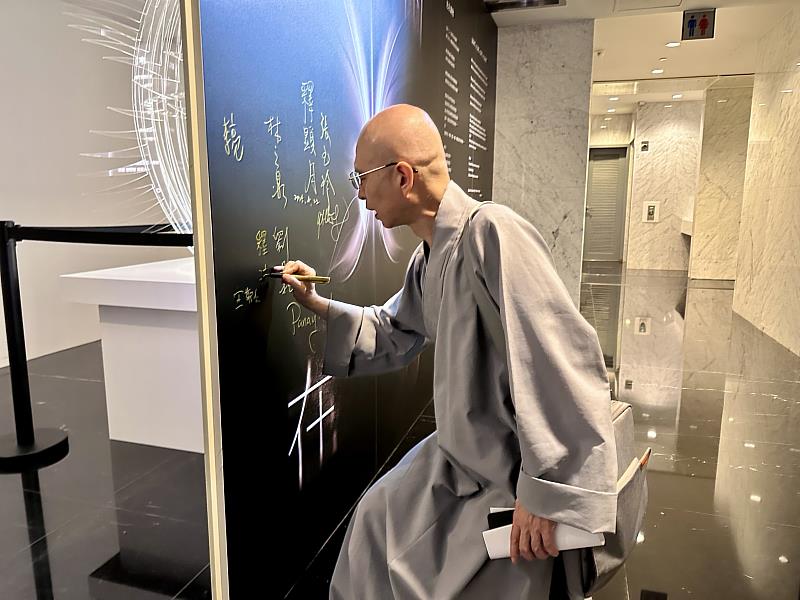 法源法師在「光在萬物」特展展板上簽名。（圖由世界宗教博物館提供）