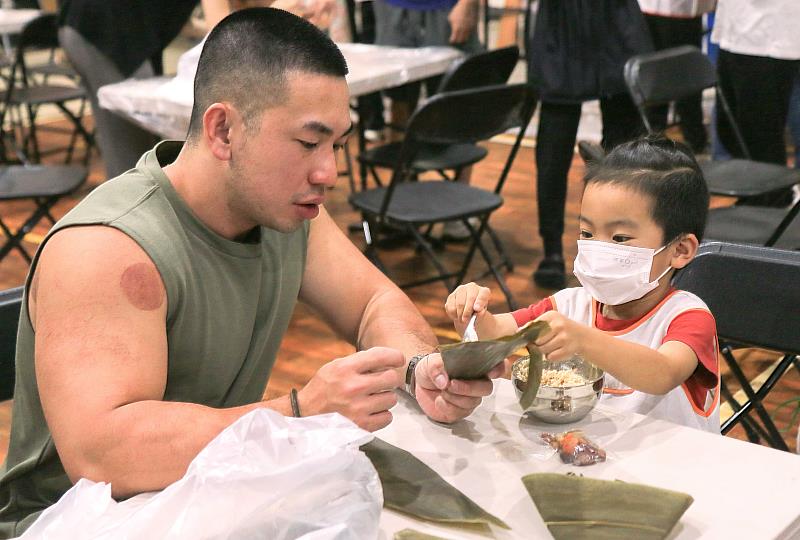 幼童父親耐心地陪同與協助孩子體驗如何包粽子。