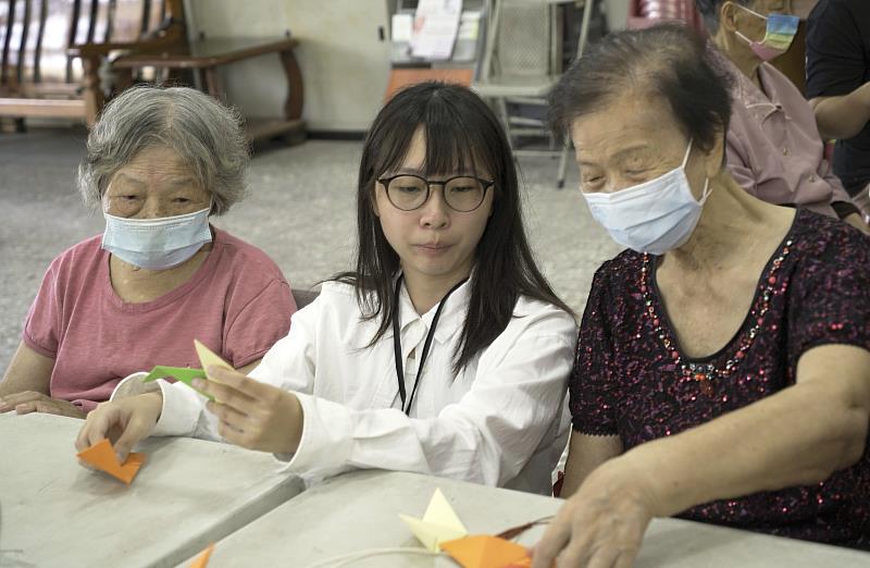 學生協助長輩學習紙摺粽子的作法