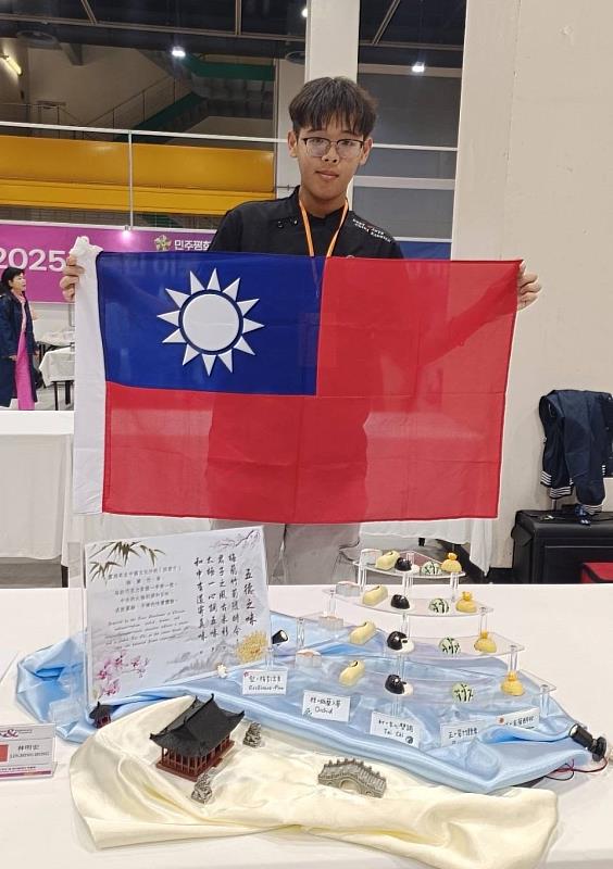 亞大護理系林明宏同學拿國旗，與他的得獎作品「五德之味」合影。