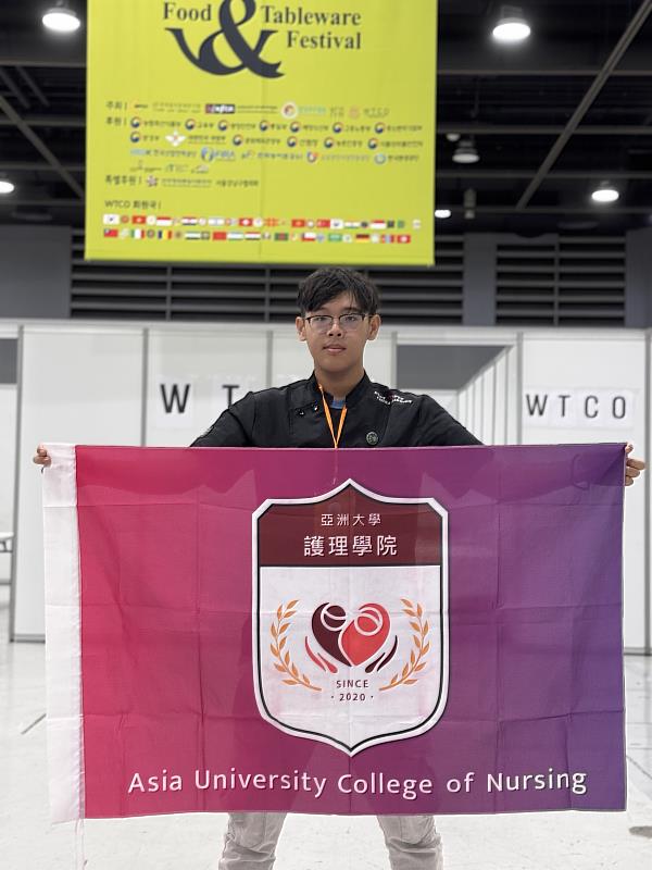 亞大護理系林明宏同學，在韓國首爾aT會展中心高舉護理學院院旗。
