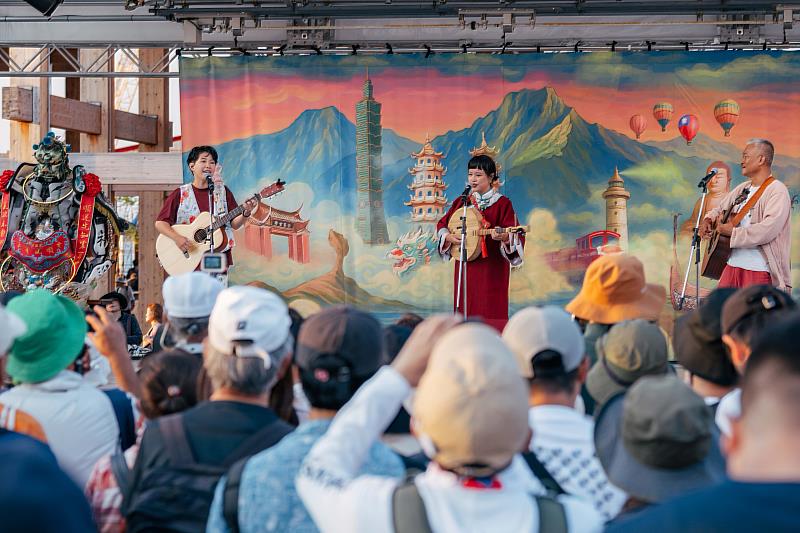 「島嶼之聲—廟埕前的謝神戲」舞台背板以玉山為主體，呈現臺南孔廟、野柳女王頭、臺北101、高雄龍虎塔等著名地景，其中最大亮點為以臺灣國旗設計、升空高飛的熱氣球。圖為客語創作歌手邱舒（左）、月琴彈唱歌者張雅淳（中）、金曲歌王謝銘祐（右）攜手演出「咱講的話：阿母的話」。